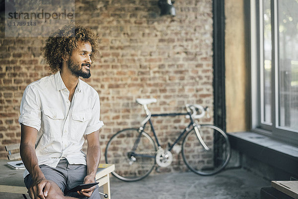 Lächelnder junger Mann mit Tablette und Fahrrad im Hintergrund