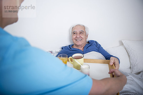 Gereatrische Krankenschwester bringt Tee ans Patientenbett