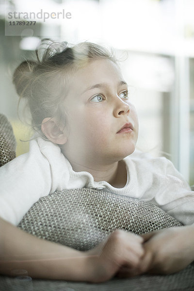 Porträt eines ernsthaften kleinen Mädchens,  das aus dem Fenster schaut.