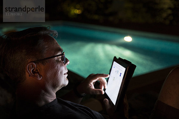 Mann mit Tablette am Pool bei Nacht