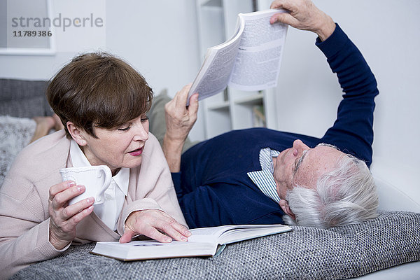 Seniorenpaar auf der Couch liegend,  Bücher lesend