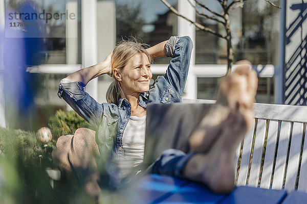 Lächelnde Frau mit Laptop zum Entspannen auf der Gartenbank