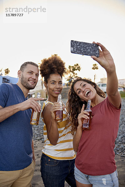 Drei Freunde mit Bierflaschen,  die Selfie am Strand mitnehmen.