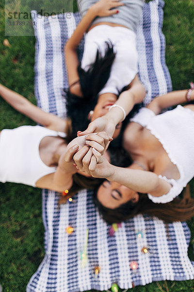 Freunde in einem Park,  die auf einer Decke liegen und ihre Arme heben.