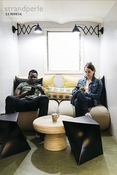 Zwei junge Profis,  die mit ihren Smartphones eine Pause im Lehrerzimmer machen.