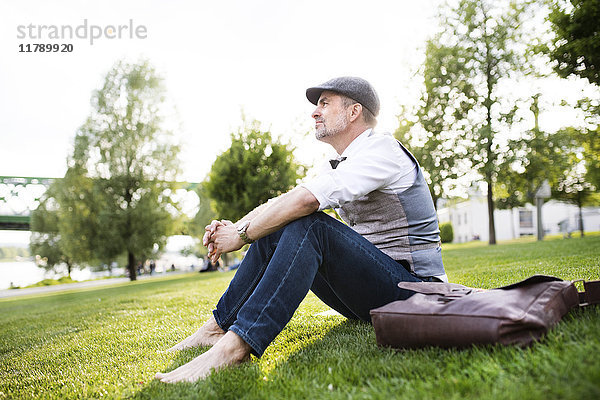 Erwachsener Geschäftsmann im Stadtpark auf Gras sitzend