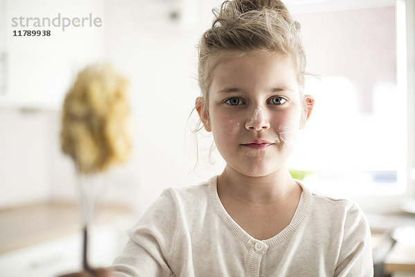 Porträt des lächelnden Mädchens in der Küche mit Teig im Gesicht