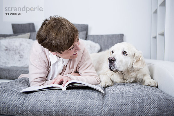 Seniorin auf der Couch liegend,  Lesebuch mit Hund an der Seite