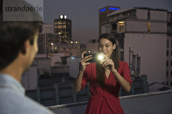 Junge Frau fotografiert Freunde auf einer Dachparty