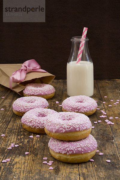 Doughnuts mit rosa Puderzucker und einer Flasche Milch auf Holz