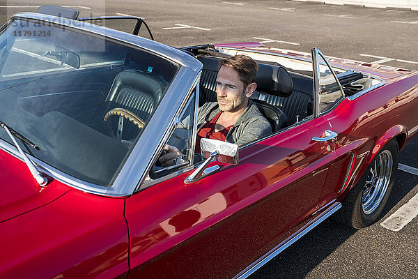 Erwachsener Mann in seinem roten Sportwagen.