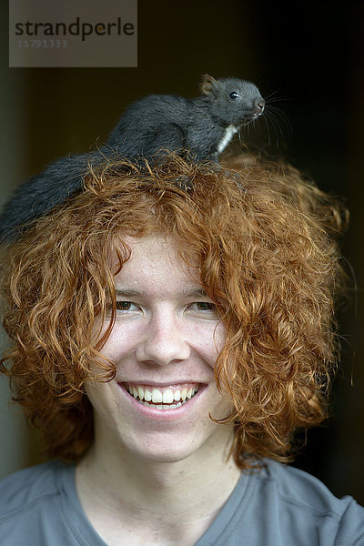 Porträt eines fröhlichen rothaarigen Teenagers mit Eichhörnchen auf dem Kopf