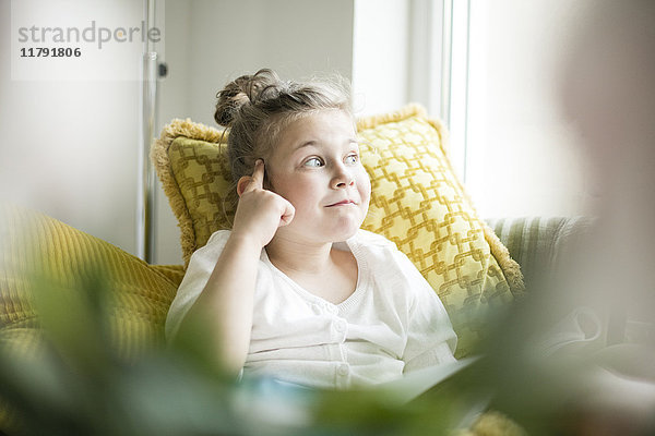 Porträt eines denkenden kleinen Mädchens sitzend mit Zeitschrift auf Sessel