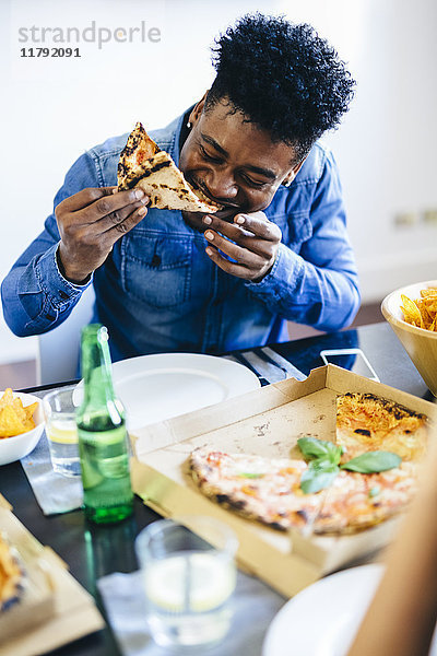 Junger Mann genießt Pizza am Esstisch