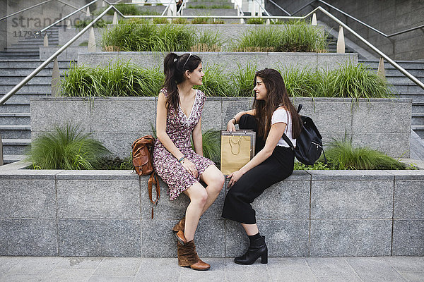 Zwei junge Frauen,  die in der Stadt sitzen und reden.