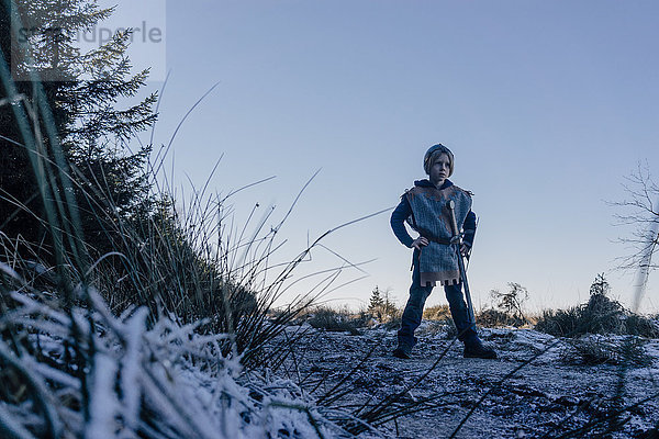 Kleiner Junge,  der auf einem Hügel steht und in Ritterkostüm spielt.