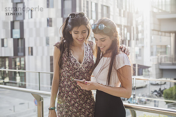 Zwei lächelnde junge Frauen beim Blick auf das Handy in der Stadt