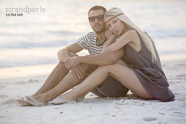 Junges Paar am Strand sitzend,  umarmend