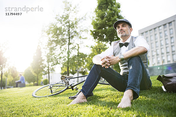 Erwachsener Geschäftsmann mit Fahrrad im Stadtpark auf Gras sitzend