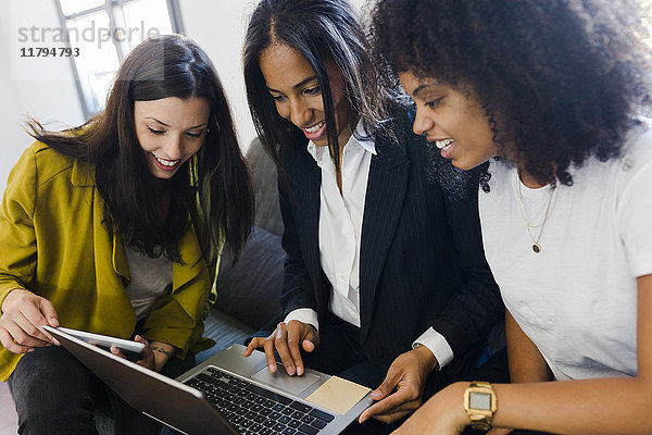 Drei lächelnde Geschäftsfrauen teilen sich den Laptop im Büro