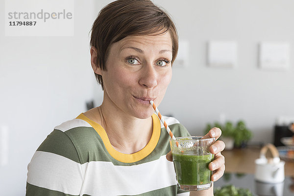 Porträt einer Frau,  die in der Küche einen grünen Smoothie trinkt.