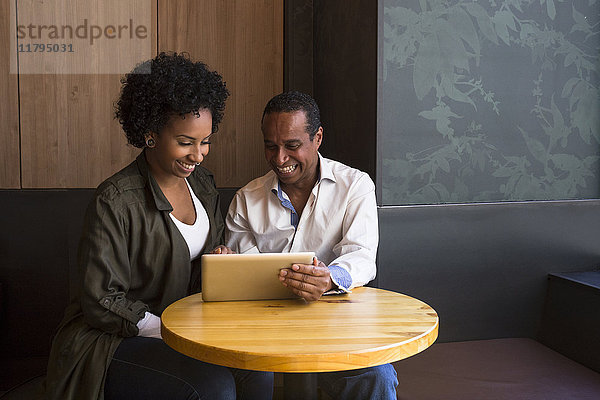 Vater und erwachsene Tochter sitzen in einem Café und haben Spaß mit der Tablette