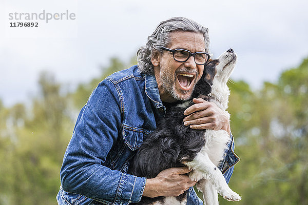 Porträt eines glücklichen älteren Mannes,  der seinen Hund kuschelt.