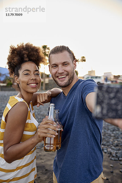 Zwei Freunde mit Bierflaschen,  die Selfie am Strand mitnehmen.