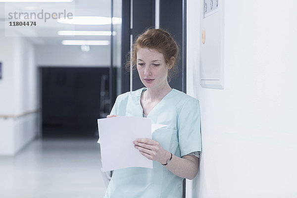 Junge Krankenschwester liest Krankenblätter und lehnt sich an die Tür