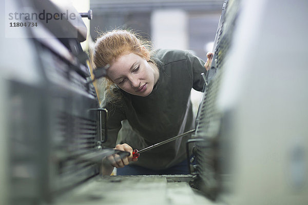 Druckereiarbeiter repariert Druckmaschine mit Schraubenzieher