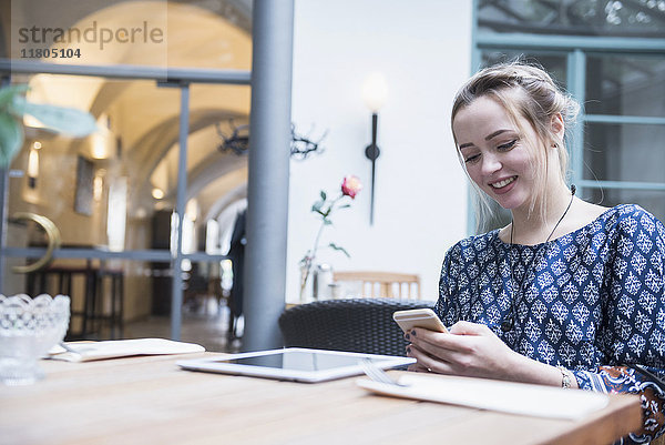 Lächelnde junge Frau,  die in einem Restaurant sitzt und mit ihrem Handy Nachrichten schreibt