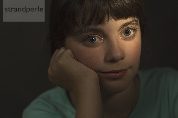 Porträt eines Mädchens,  das mit der Hand auf dem Kinn auf grauem Hintergrund ruht.