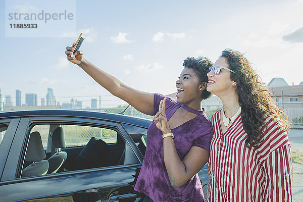 Glückliche junge Frau nimmt Selfie mit Freundin mit dem Auto gegen den Himmel,  Los Angeles,  Kalifornien,  USA