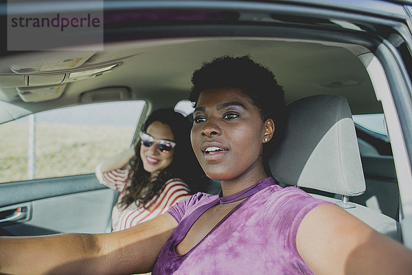 Junge Frau sitzt mit Freundin im Auto und schaut weg,  während sie an einem sonnigen Tag im Auto sitzt.