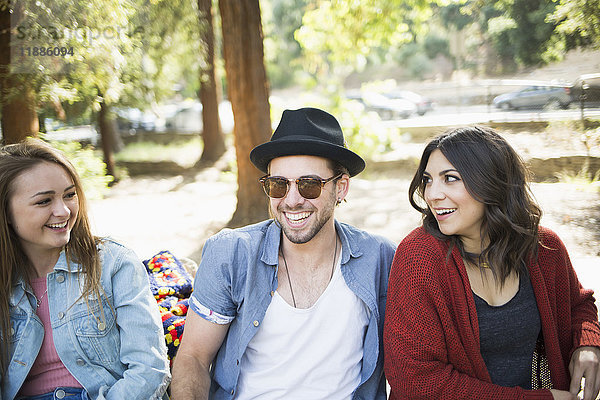 Glückliche männliche und weibliche Freunde sitzen auf einer Bank im Park.