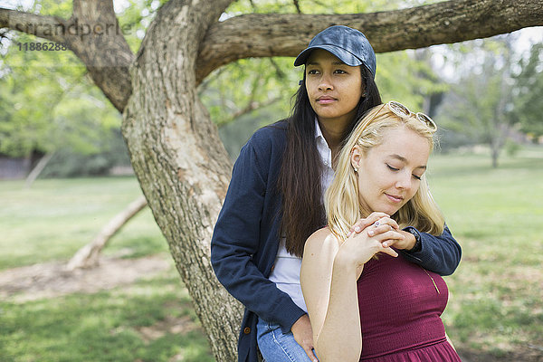 Junges lesbisches Paar sitzend am Baumstamm im Park