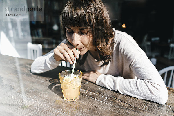 Frau sitzt im Café und trinkt einen Drink mit einem Strohhalm.