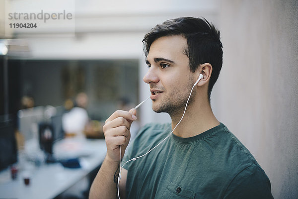 Junger männlicher Programmierer mit In-Ear-Kopfhörer beim Sprechen im Büro