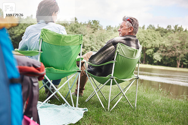 Älteres Paar sitzt in Campingsesseln am See,  Rückansicht