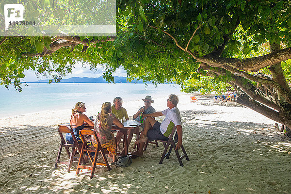 Freunde entspannen sich am Esstisch am Strand,  Koh Rang Yai,  Thailand,  Asien