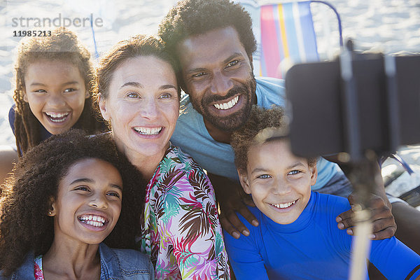 Lächelnde,  fröhliche multiethnische Familie,  die Selfie mit Selfie-Stick-Kamera-Handy am Strand nimmt.