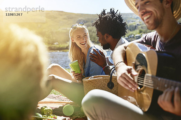 Junge Freunde spielen Gitarre und genießen sonniges Sommerpicknick