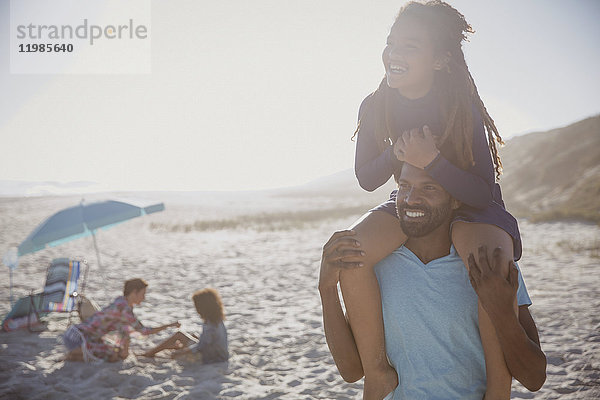 Lächelnder Vater mit Tochter auf den Schultern am sonnigen Sommerstrand