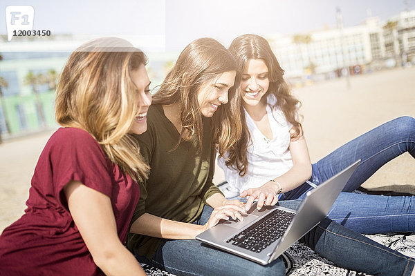 Drei glückliche Freundinnen mit einem Laptop am Strand