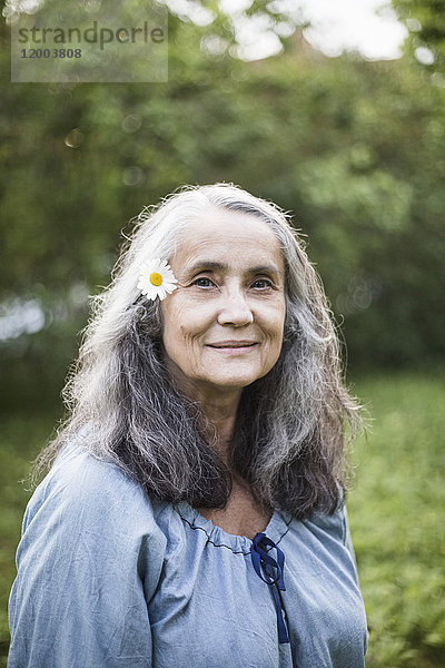 Porträt der lächelnden Seniorin mit Gänseblümchen im Hinterhof