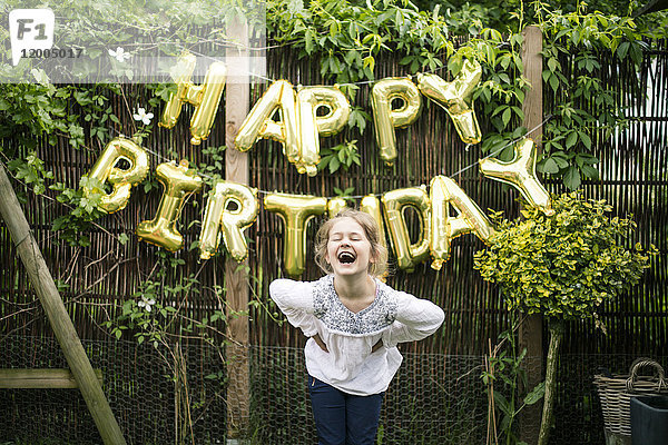 Porträt des lachenden Mädchens im Garten mit Dekoration für die Geburtstagsparty im Hintergrund