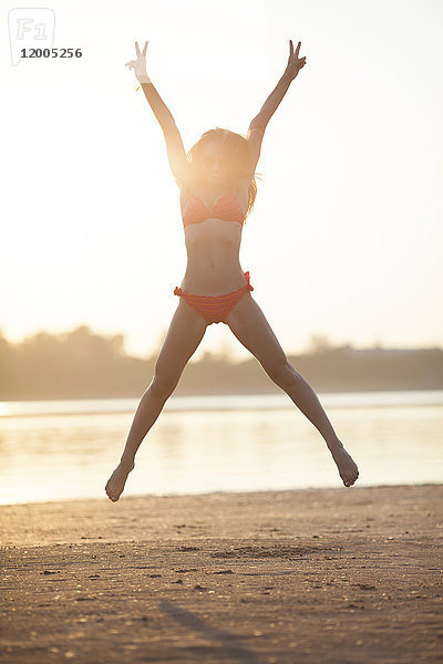 Fröhliche junge Frau beim Springen am Strand