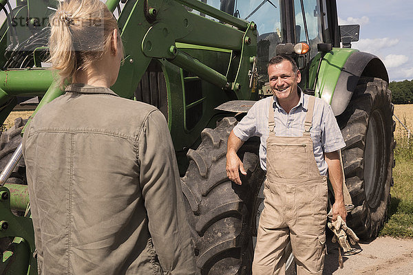 Männlicher Bauer im Gespräch mit einer Frau,  während er an einem sonnigen Tag an einer Landmaschine steht.