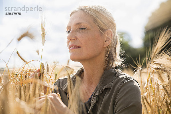 Nachdenklich lächelnde Frau beim Anblick der Weizenähren auf dem Bauernhof an einem sonnigen Tag.