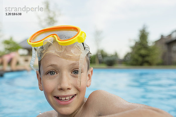 Porträt eines lächelnden Jungen ohne Hemd mit Schwimmbrille im Pool